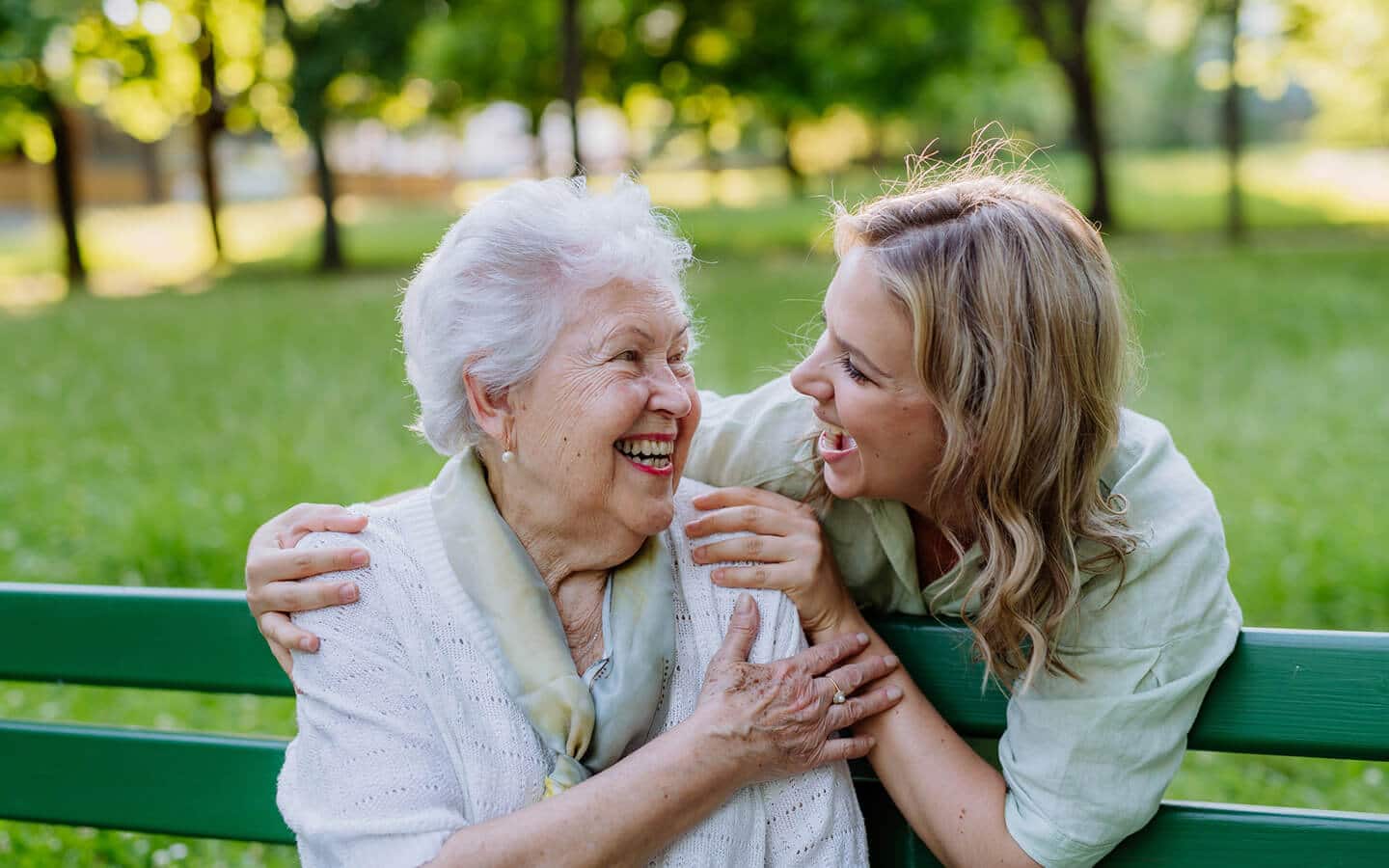 young woman embracing an older woman seated on a park bench