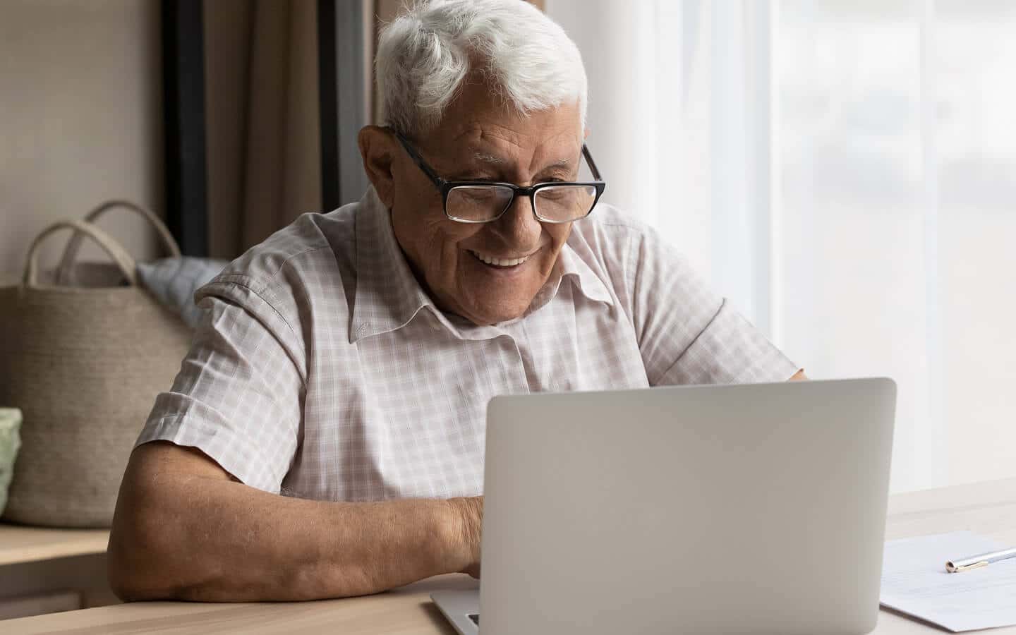 Senior man wearing glasses smiling and looking at a laptop computer