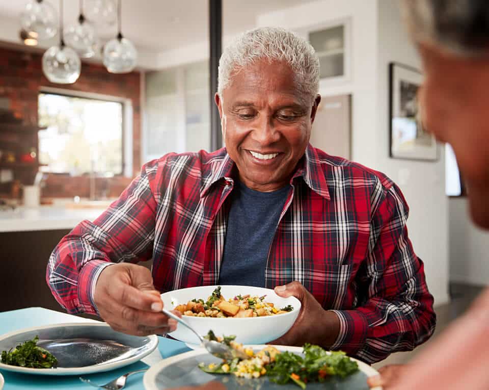 Senior man dishing food out of a bowl onto a plate