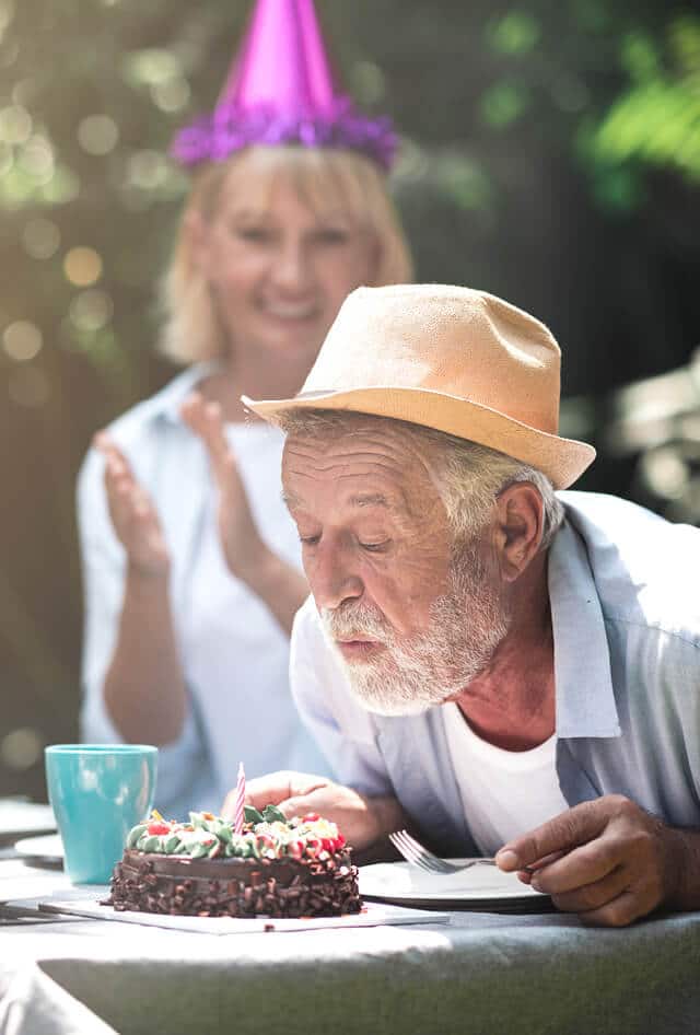 Older man wearing a hat who is blowing out a birthday candle