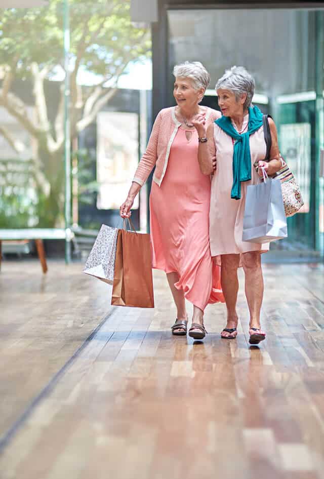 Two senior ladies dressed in pink and holding shopping bags walking