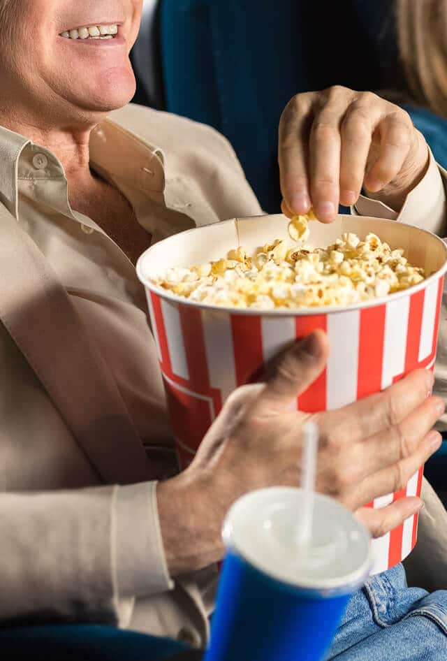 Man seated while holding bucket of popcorn