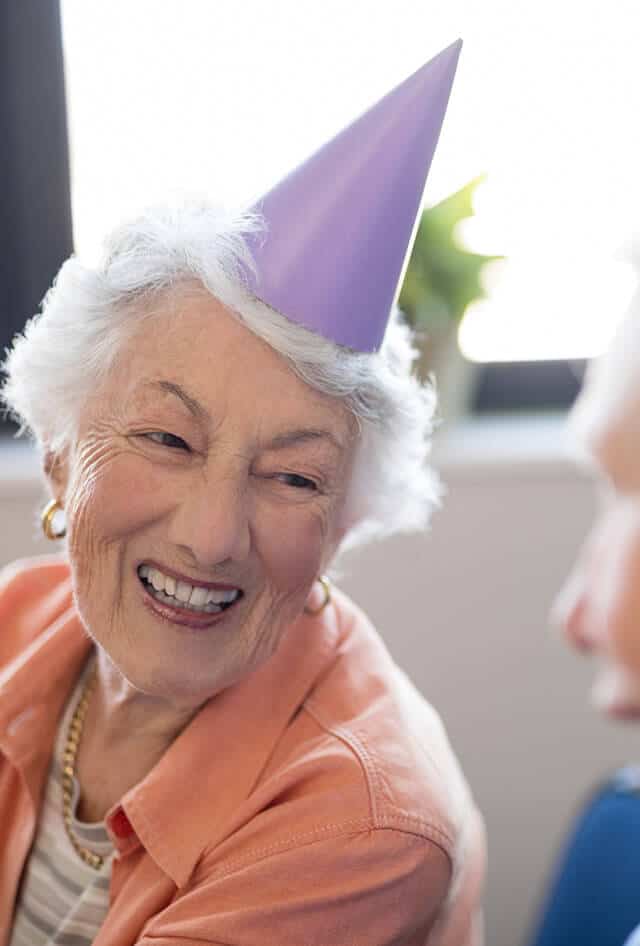 Senior lady wearing a purple birthday hat and smiling