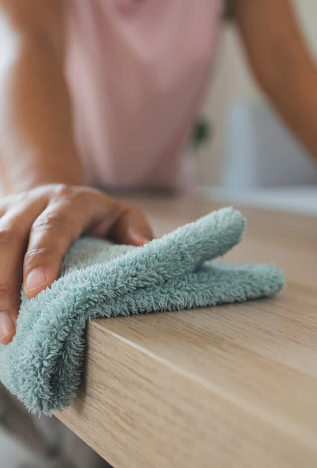 Hands holding a green cleaning cloth and wiping a counter